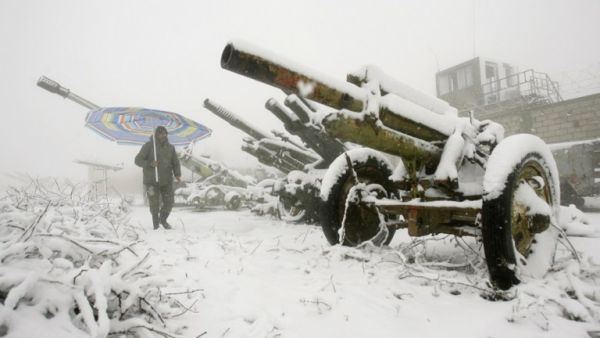 A Lebanese man holding a umbrella walks past abandoned Israeli cannons during a snow storm in the southern village of Khiam, on the Israeli-Lebanese border. [AFP]