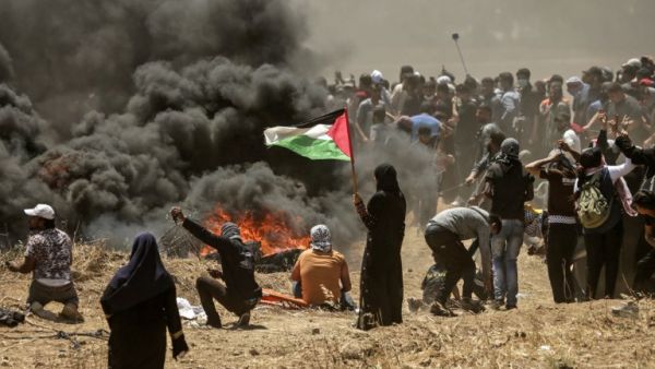 A Palestinian woman holding her national flag looks at clashes with Israeli forces near the border between the Gaza strip and Israel east of Gaza City on May 14, 2018. (MAHMUD HAMS/ AFP) A Palestinian woman holding her national flag looks at clashes with Israeli forces near the border between the Gaza strip and Israel east of Gaza City on May 14, 2018. (MAHMUD HAMS/ AFP)