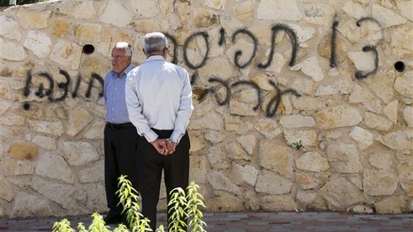 Arab Israeli men stand next to graffiti reading in Hebrew "Arabs Out" on the wall of a mosque in the northern Israeli city of Umm al-Faham on April 18, 2014. (AFP/ File Photo)