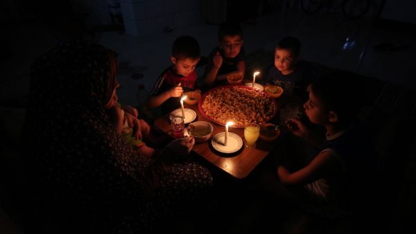 A Palestinian family eats dinner by candlelight at their makeshift home in the Rafah refugee camp, in the southern Gaza Strip, during a power outage on June 11, 2017. (Said Khatib/AFP)