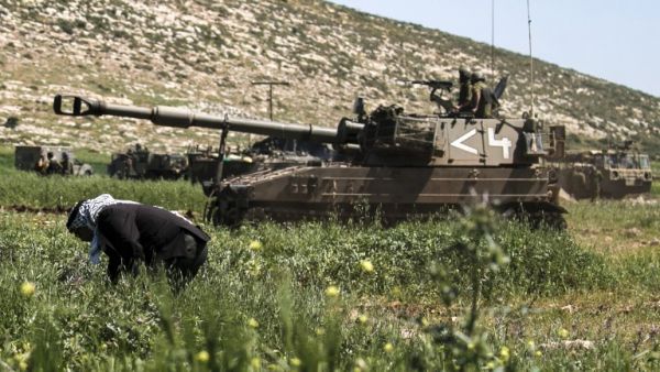 Israeli soldiers drive a 155mm self-propelled howitzer past a Palestinian farmer during a military exercise near the West Bank village of Aqraba, east of Nablus, on April 4, 2017. (AFP/Jaafar Ashtiyeh)