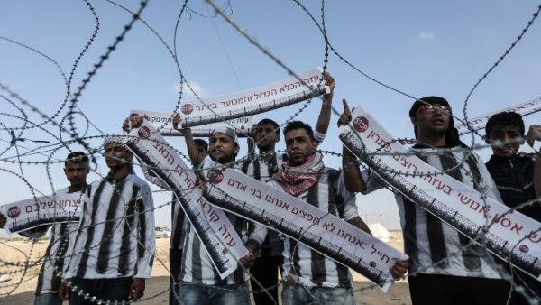Palestinian demonstrators dressed in striped t-shirts marking internment camp outfits hold up signs with slogans written in Hebrew/AFP