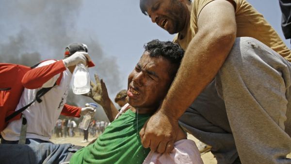 A Palestinian man assists a wounded protestor during clashes with Israeli security forces near the border between Israel and the Gaza Strip/AFP