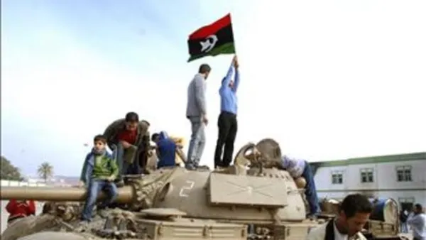 يبيون يرفعون علماً وطنياً قديماً فوق دبابة في مجمع أمني في بنغازي