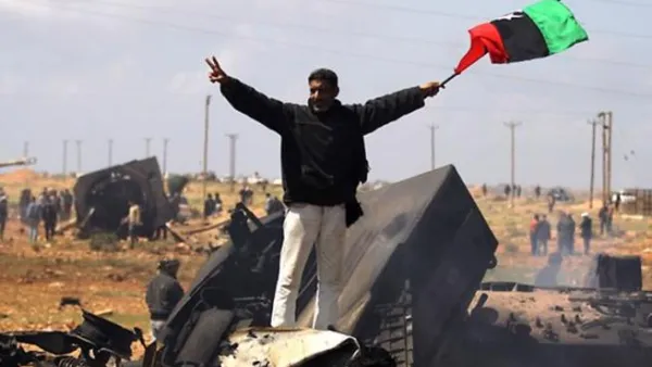 ليبي يرفع علم المعارضة على حطام آليات جيش القذافي