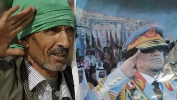 احد انصار القذافي يحمل لوحة له في الزي العسكري