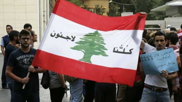 Lebanese protesters hold a Lebanese national flag on which is written in Arabic, "We are all refugees" on July 18, 2016 in the capital Beirut. (AFP/Joseph Eid)