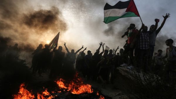 Palestinian protesters wave national flags as they stand near burning tyres during a demonstration on the beach near the maritime border with Israel. (MAHMUD HAMS / AFP)