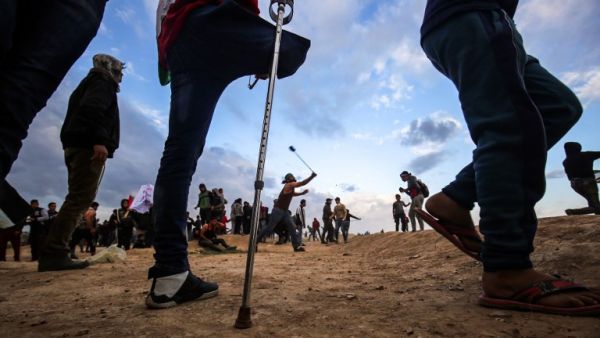 A Palestinian amputee stands by as others protest and use slingshots to hurl objects during clashes following a demonstration along the border with Israel. (SAID KHATIB / AFP)