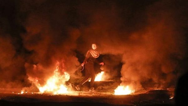 A masked Palestinian demonstrator pulls a burning tire during a night demonstration near the fence along the border with Israel, east of Gaza City, on February 11, 2019. (AFP/ File)
