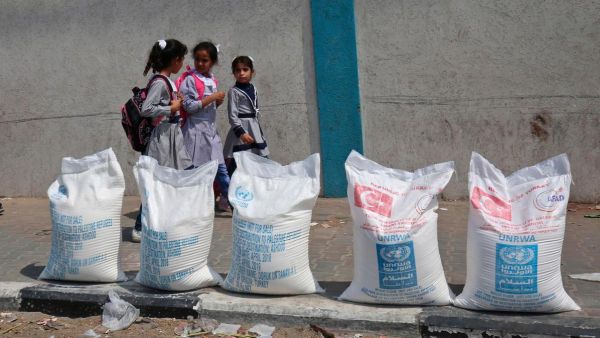 Palestinian school girls walk past sacks of flour outside a UN compound at the Rafah refugee camp in the southern Gaza Strip. (AFP/ File)
