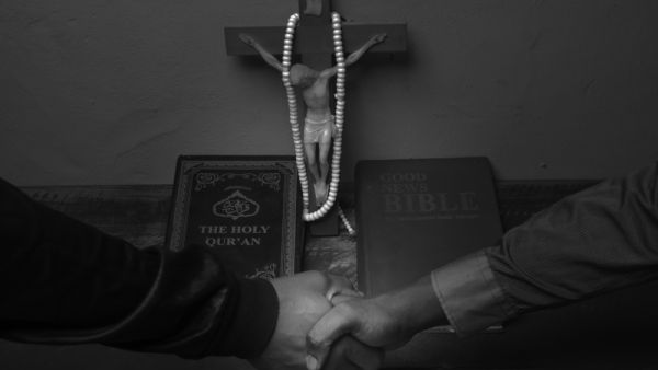 Christian and Muslim handshake over a Holy Bible and Quran. (Shutterstock)
