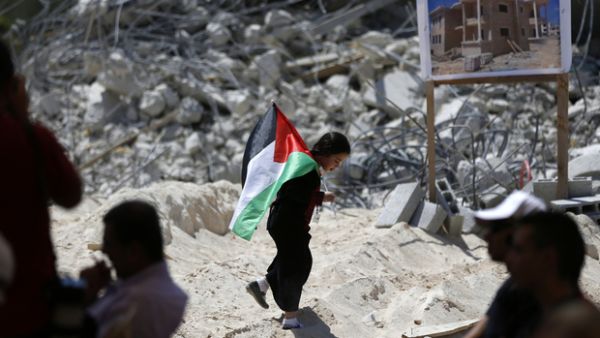 A Palestinian child holds a national flag as she walks past the rubble of Palestinian homes destroyed by Israeli authorities on July 29, 2016. (AFP/File)