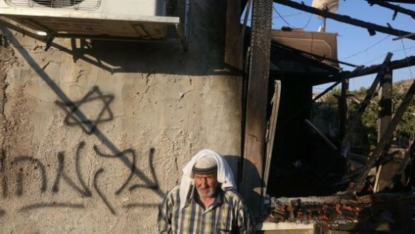 A Palestinian man stands next to a graffiti reading "Revenge," after a house was set on fire by Jewish settlers in the West Bank, July 31, 2015. (AFP/File)