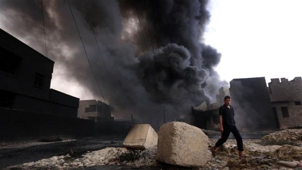 An Iraqi man walks near smoke billowing from oil wells, set ablaze by Daesh militants before fleeing the oil-producing region of Qayyarah, on August 30, 2016. (AFP/File)