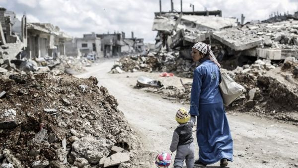 A Kurdish Syrian woman walks with her child past the ruins of the town of Kobane. (AFP/Yasin Akgul) 