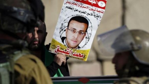 A protester holds up a poster of Mohammed Al Qiq as Israeli soldiers look on. (AFP/File)