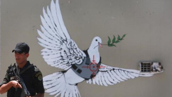 An Israeli solider stands by iconic Banksy grafitti on the Israeli separation barrier that runs through Bethlehem. Getty Photo 