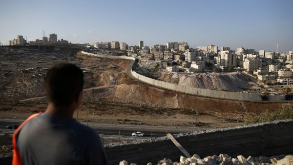 A picture taken on October 18, 2016 from the east Jerusalem Arab neighbourhood of Issawiya shows a Palestinian youth looking on as the Palestinian Shuafat refugee camp (R) is seen behind the controversial Israeli separation wall. (AFP/Ahmad Gharabli)