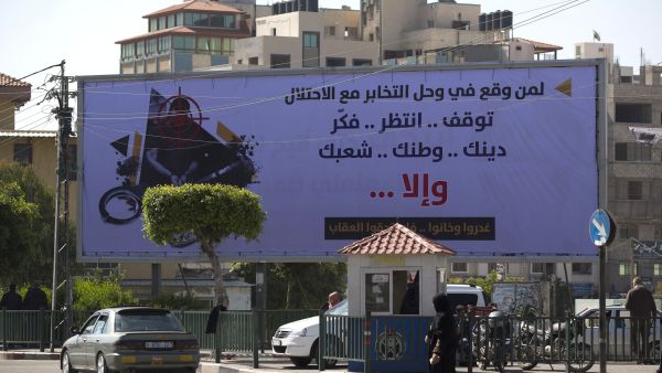 A woman walks past a billboard in Gaza put up by the Hamas authorities warning collaborators to stop their activities. (AFP/Mohammed Abed)