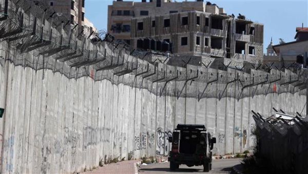 An Israeli police car patrols along a section of Israel’s Apartheid Wall that separates the West Bank city of al-Ram (L) from east al-Quds (Jerusalem) (R) on February 24, 2016. (AFP)