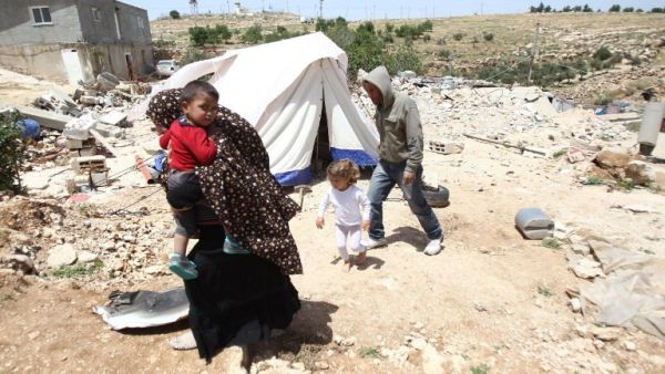 A Palestinian family, whose house was demolished by Israeli bulldozers, walk past a tent on April 21, 2015 in the southern West Bank. (AFP/File) 