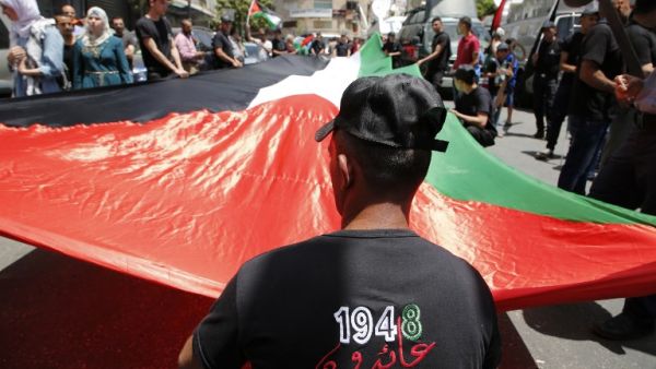 Palestinian protesters hold a large national flag as they take part in a protest marking the 69th anniversary of Nakba, near the West Bank city of Ramallah on May 15, 2017. (AFP/Abbas Momani)