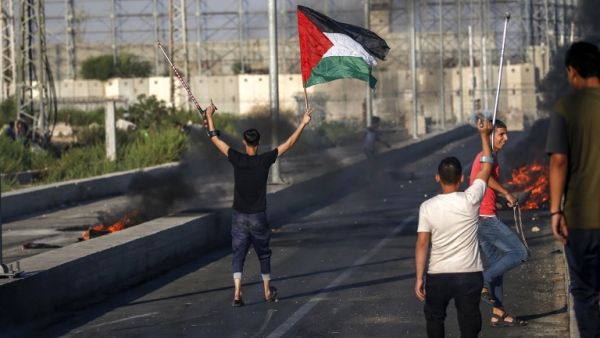 A Palestinian protester holds up a Palestinian flag in one hand while raising a crutch with another during clashes with Israeli forces near Gaza Strip on September 26, 2018. (SAID KHATIB / AFP) A Palestinian protester holds up a Palestinian flag in one hand while raising a crutch with another during clashes with Israeli forces near Gaza Strip on September 26, 2018. (SAID KHATIB / AFP)