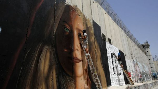 Italian artist Jorit Agoch (L) paints mural depicting jailed Palestinian teenager Ahed Tamimi next to another artist on Israel's controversial separation barrier in the West Bank city of Bethlehem, July 25,2018 (AFP/ File)
