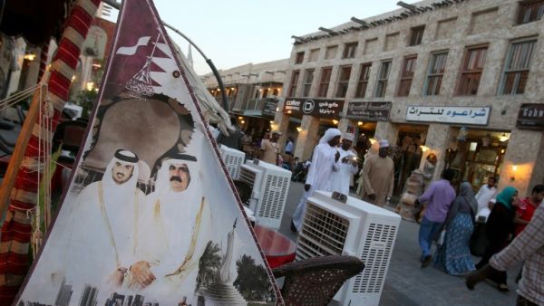 This file photo taken on June 25, 2014 shows people walking past a banner bearing portraits of former emir of Qatar Sheikh Hamad bin Khalifa al-Thani (R) and his son current leader Sheikh Tamim bin Hamad al-Thani displayed at Souq Waqif in the Qatari capital Doha. (Karim Jaafar/AFP)
