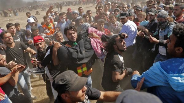 Palestinians carry a demonstrator injured during clashes with Israeli forces near the border between the Gaza strip and Israel east of Gaza City on May 14, 2018/AFP