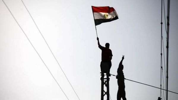 Protestor waves a flag as another makes the victory sign at the top of a Cairo electricity pole (AFP)