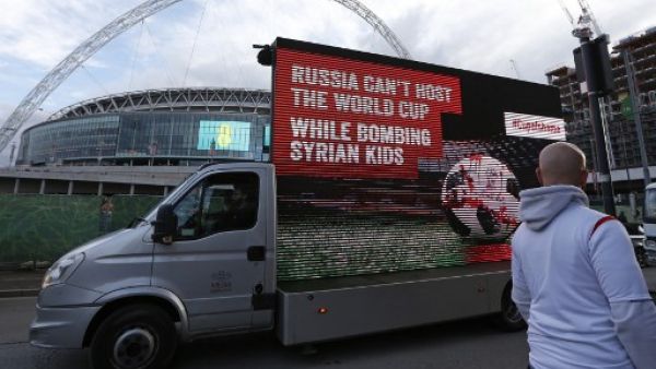 A mobile billboard showing a design of a blood-stained football on a pitch, with the words "Russia can’t host the World Cup while bombing Syrian kids", is driven past Wembley Stadium ahead of the International friendly football match between England and Italy in London on March 27, 2018.
Ian KINGTON / AFP