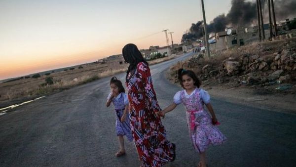 A woman walks with two children, looks back at smoke billowing in Idlib province (AFP)