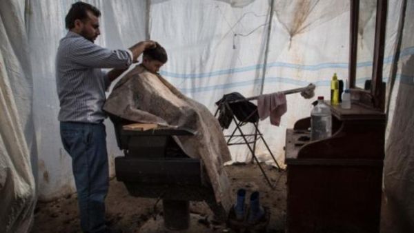 طفل سوري يقص شعره في محل حلاقة بمخيم اعزاز شمال سوريا/أ.ف.ب