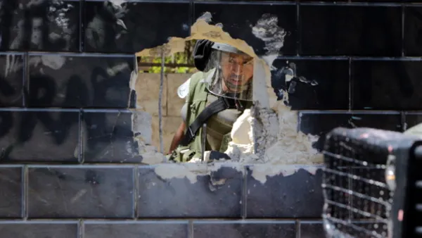 Israeli security guard peering through a hole of Israel's  separation barrier by Palestinian youth in the Abu Dis neighrbood, bordering Jerusalem on July 9, 2013. [Abbas Momani/Getty Images]