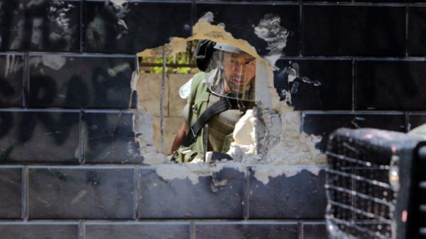 Israeli security guard peering through a hole of Israel's  separation barrier by Palestinian youth in the Abu Dis neighrbood, bordering Jerusalem on July 9, 2013. [Abbas Momani/Getty Images]