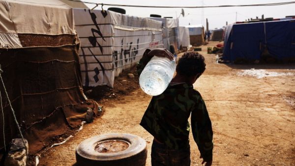 A displaced Syrian child walks through a camp with a jug of water in a makeshift camp for Syrian refugees only miles from the border with Syria in the Bekaa Valley on November 12, 2013 in Majdal Anjar, Lebanon. [Spencer Platt/ Getty Images]