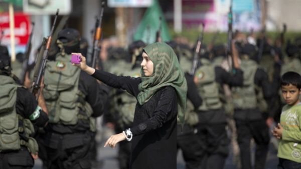 A Palestinian girl takes a photo of masked militants of Ezzedine al-Qassam Brigades, Hamas's armed wing, using her mobile phone as they parade in Jabalia refugee camp, northern Gaza Strip, on November 14, 2013, during an anti-Israel march as part of the celebrations marking the first anniversary of Israel's Operation 'Pillar of Defence'. [MOHAMMED ABED/AFP/Getty Images]