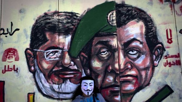 Egyptian protester wears a Guy Fawkes mask while posing for a photo next to a mural painted overnight on the exterior wall of the presidential palace depicting president Mohammed Morsi, left, former military council ruler Hussein Tantawi, center and ousted President Mubarak with Arabic that reads "No, the brotherhood's constitution is not valid, in Cairo. [AP Photo/Nasser Nasser