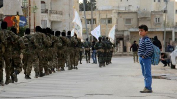 A Syrian boy looks at rebel fighters from the Jaish al-Fatah (or Army of Conquest) brigades marching through the northwestern city of Idlib in March 2017. (AFP)