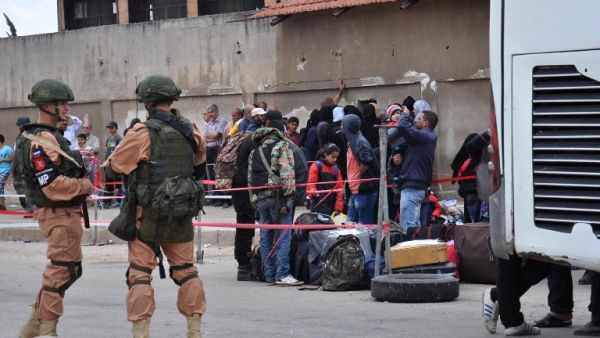 Russian troops (L) stand guard as Syrian opposition fighters and their families board a bus at a checkpoint manned by regime forces ahead of their evacuation on May 20, 2017. (Stringer/AFP)