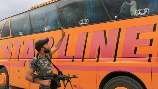 A rebel fighter waves at civilian arriving by bus in al-Bab, in the northern province of Aleppo, after leaving al-Waer, the last opposition-held neighborhood of the central city of Homs, on May 5, 2017. (AFP/Zein Al Rifai)