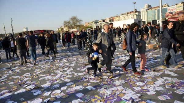 A man and a woman hold each other a child by the hand as they walk on leaflets reading "yes" thrown on the ground at the Kadikoy district, in Istanbul, after the start of the election banning, on April 15, 2017, on the eve of the constitutional referendum. (AFP/Bulent Kilic)