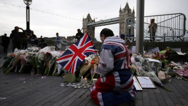 A man holds a Union flag as he kneels near flowers layed at Potters Fields Park in London on June 5, 2017, during a vigil to commemorate the victims of the terror attack on London Bridge and at Borough Market that killed seven people on June 3. (AFP/Daniel Leal-Olivas)