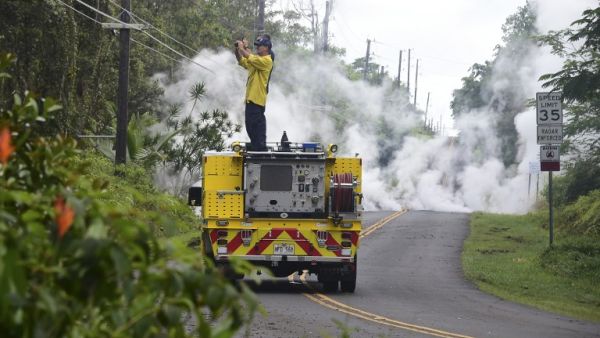 A firefighter takes photos near steam rising from a fissure in Leilani Estates subdivision on Hawaii's Big Island on May 4, 2018. (FREDERIC J. BROWN / AFP)