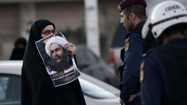 A woman holds a picture of the executed Shia cleric Nimr al-Nimr infront of a Saudi policeman during a protest. (AFP/File)