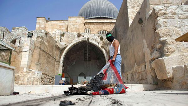 A masked Palestinian wearing a Hamas headband takes a burnt carpet out of Al-Aqsa mosque in Jerusalem's Old City during clashes at the compound. (AFP/File)