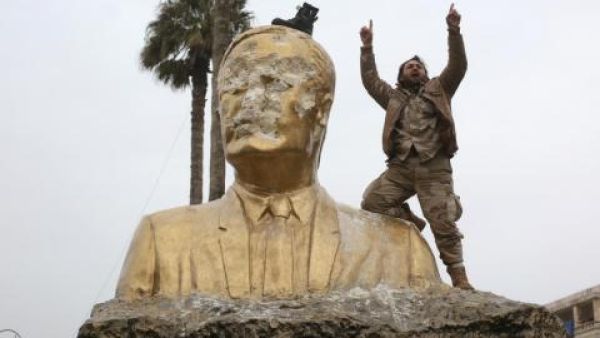 A militant from the Army of Conquest alliance destroys a statue of Bashar al-Assad in Syria's Idlib Province. (Al Bawaba/File)