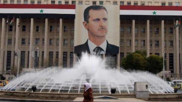 A woman walks past a banner of President Bashar Assad hanging from a Central Bank building in Damascus, Syria. (AFP/Anwar Amro)